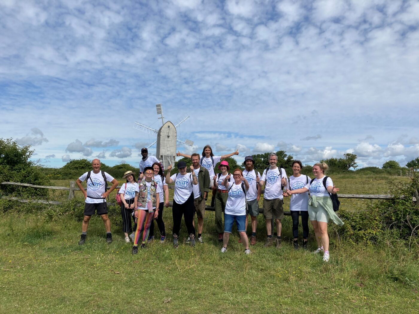 Group of hikers standing in front of a windmill in the countryside. They are all wearing Hike Against Homelessness white t-shirts.
